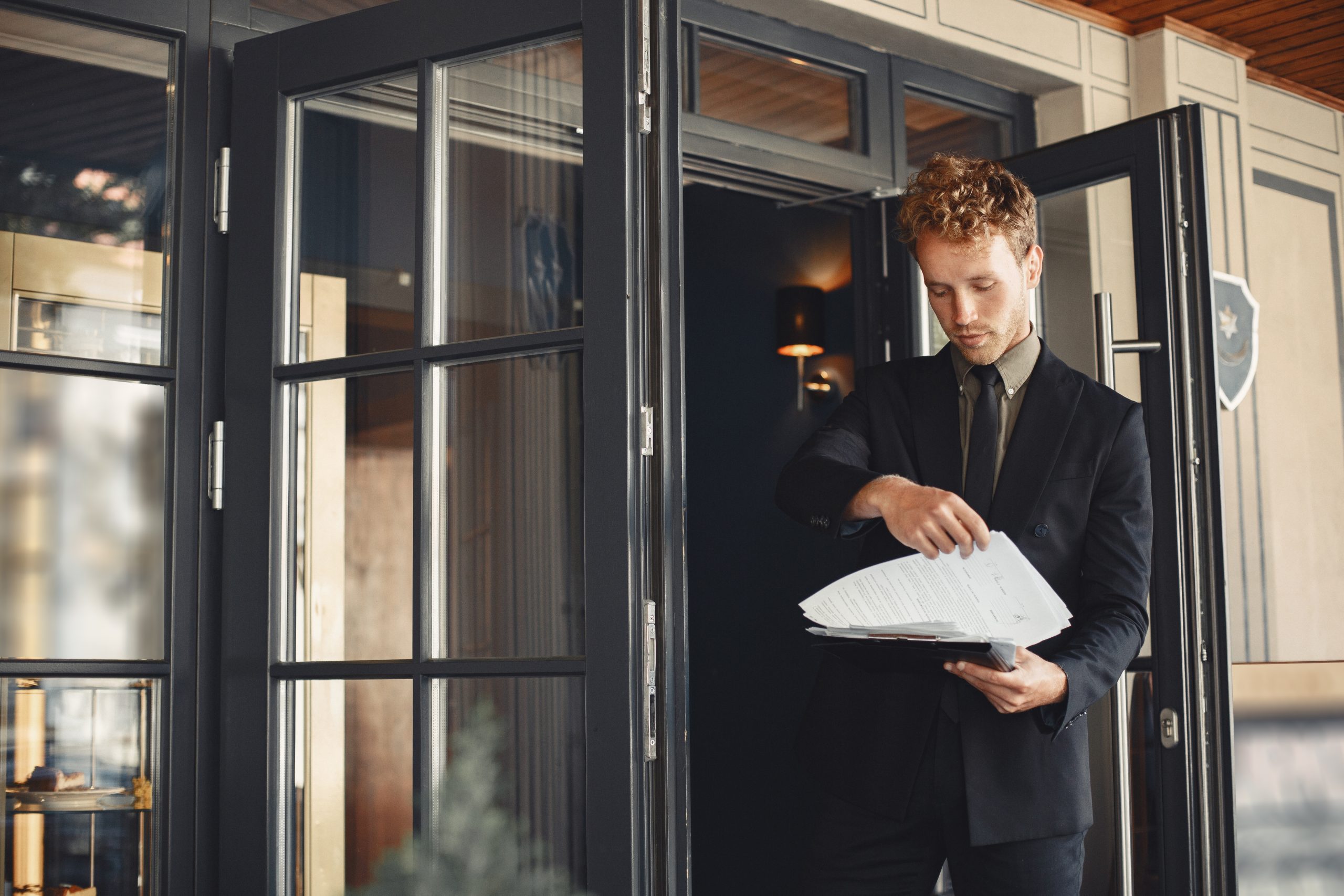 Man in business attire reviewing documents at an open door. Professional setting, focus on paperwork.